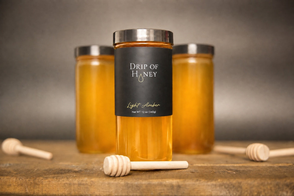 Three 12 oz jars of Drip of Honey on a wood table with honey dippers