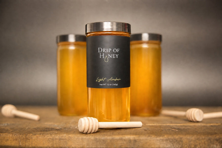 Three 12 oz jars of Drip of Honey on a wood table with honey dippers