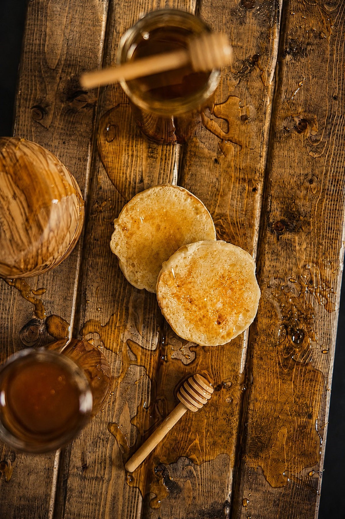 Honey pooling around warm pancakes on a weathered wood table, a jar and dipper alongside