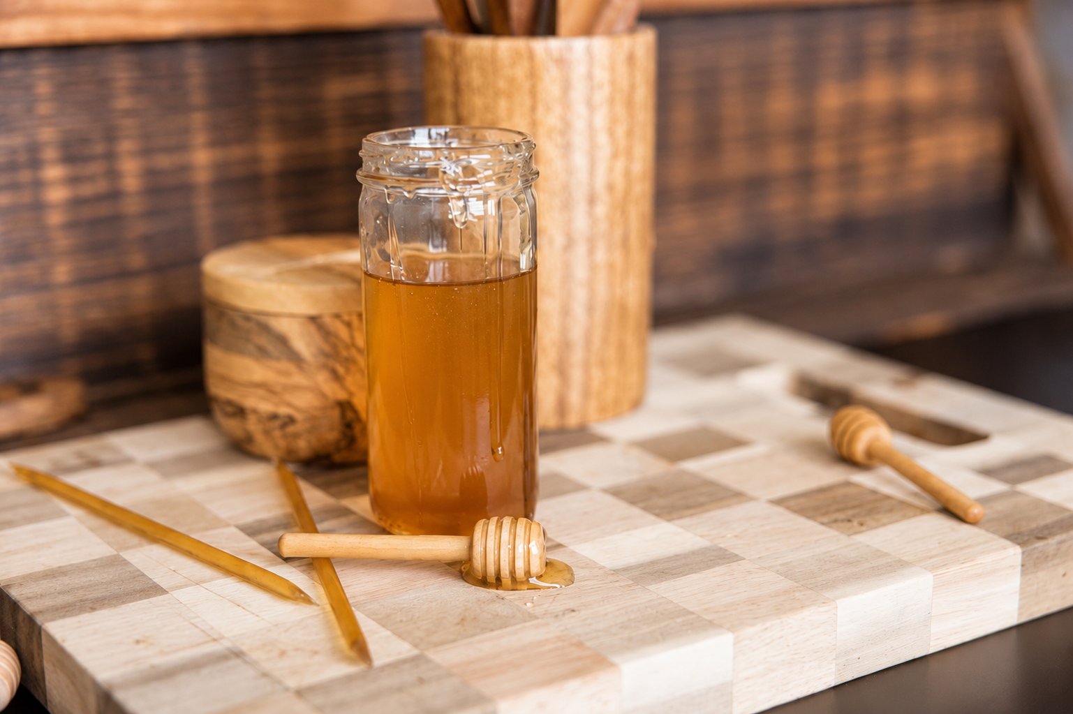 A jar of honey on a cutting board with a wooden dipper