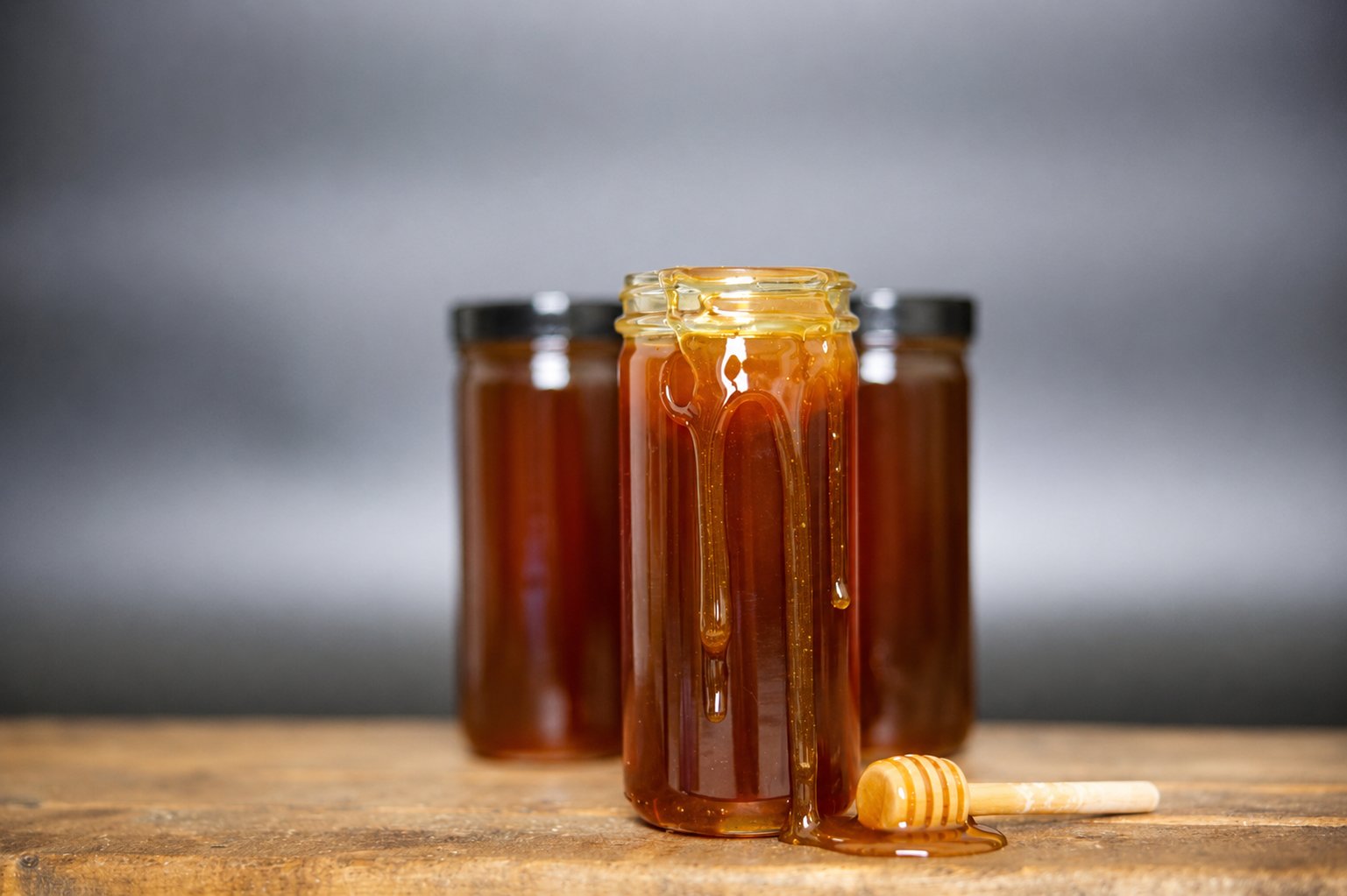 Open jar of honey dripping onto a wood board beside a dipper